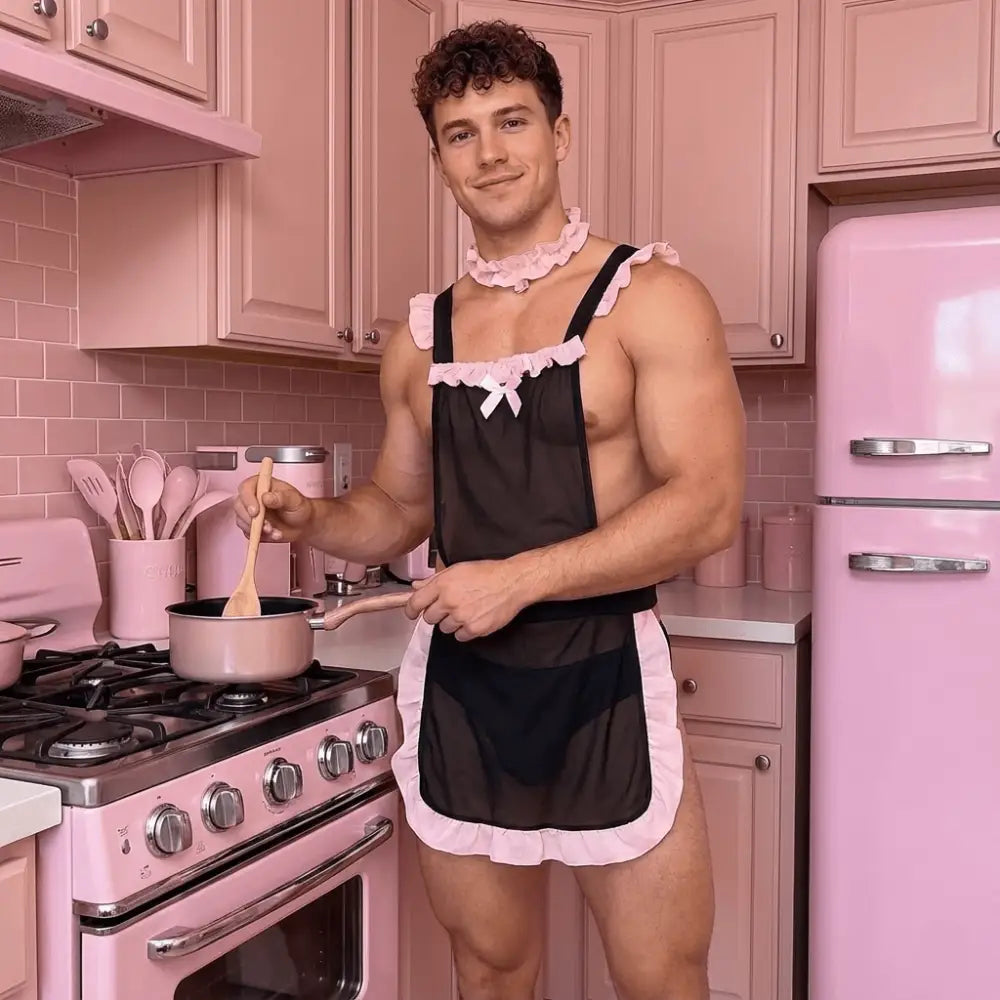 Man in a black apron with pink trim cooking in a pink kitchen.